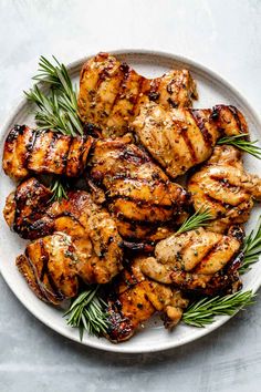 grilled chicken with rosemary garnish on a white plate, ready to be eaten