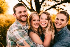 a group of friends hugging each other in front of a tree and grass covered field