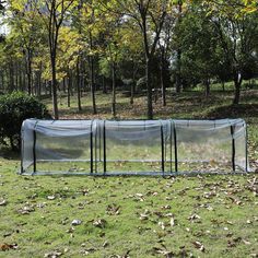 a small green house in the middle of a field with leaves on the ground and trees behind it