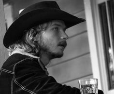 a man wearing a cowboy hat sitting at a table with a drink in front of him