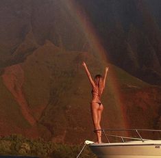 a woman standing on the bow of a boat with her arms up in the air