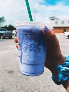 a woman holding up a blue starbucks cup with a green straw in it's hand