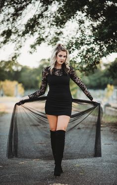 a woman in a short black dress is posing with her hands on her hips while wearing thigh high boots