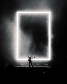 a man standing on top of a stage holding a tennis racquet under a neon light