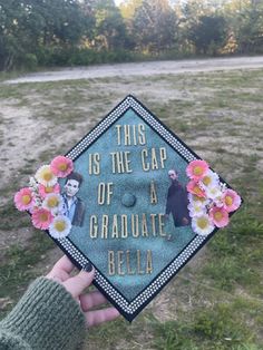 someone holding up a graduation cap with flowers on it that says, this is the cap of a graduate, belia