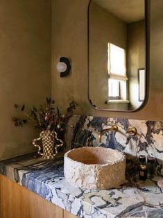 a bathroom sink with marble counter top and mirror above it, in front of a window