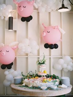 a table topped with a cake covered in pink and white balloons next to a wall