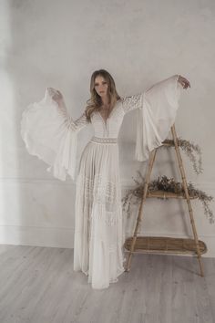 a woman standing in front of a white wall with her arms spread out and wearing a dress