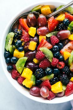 a white bowl filled with fruit salad and a fork in it's side dish