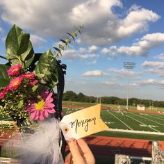 someone holding up a sign with flowers in front of a football field that says morgan