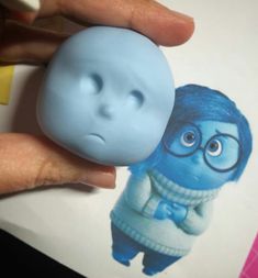 a hand holding a blue toy with glasses on it's face and an image of the character from inside out