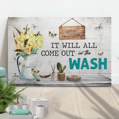 a wooden sign that says it will all come out of the wash with flowers in a vase