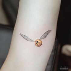 a small tattoo on the arm of a person with an orange and silver bird charm