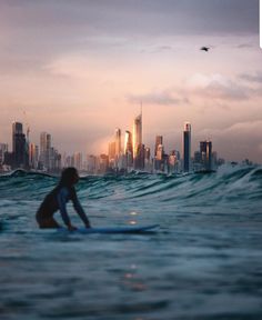 a person on a surfboard in the water with a city skyline in the background