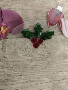 a glass bowl with holly decorations on it and purple orchids in the back ground