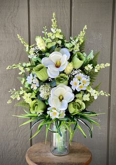 a vase filled with white and green flowers on top of a wooden table next to a wall