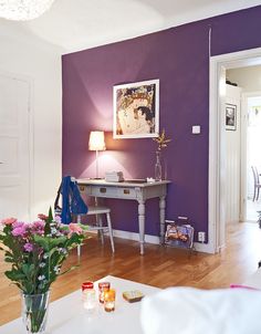 a living room with purple walls and white furniture in the center, along with flowers on the coffee table