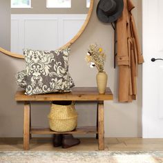 a wooden bench sitting under a round mirror next to a coat rack and vase with flowers