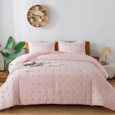 a bed with pink comforter and pillows in a room next to a potted plant