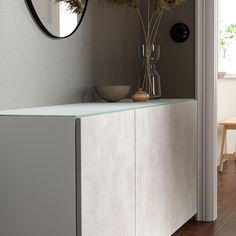 a vase with dried flowers on top of a white cabinet next to a wall mirror