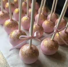 pink cake pops with gold glitter on them are lined up and tied to white sticks