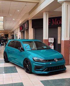 a blue car is parked in the middle of a shopping mall with people walking by