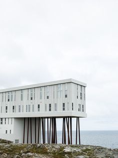 a tall white building sitting on top of a rocky hill next to the ocean with a sky background