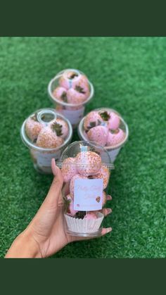 a hand holding a cupcake with pink frosting and sprinkles in it