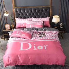 a bed with pink comforter and pillows on top of it in front of a gray wall