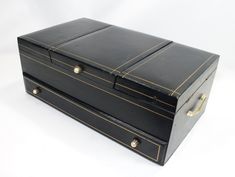 an old black leather box with gold trimmings on the inside and outside, sitting on a white surface