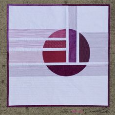 a quilted wall hanging on the side of a cement floor with purple and white stripes