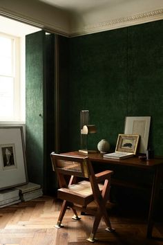 a desk with a chair and pictures on it in front of a green painted wall