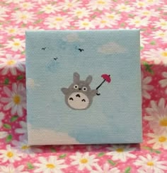 a small canvas with a hippo holding an umbrella on it's side in front of some daisies