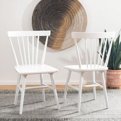 two white chairs sitting next to each other in front of a wall with a plant