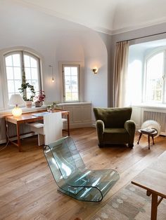 a living room filled with furniture next to two large windows on top of hard wood flooring