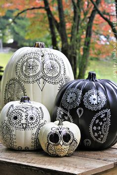 some black and white painted pumpkins sitting on a wooden table with trees in the background