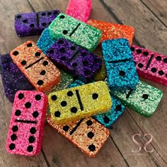 several different colored dices with black dots on them sitting next to each other in front of a wooden table