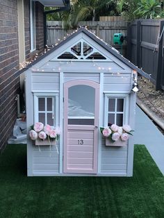 a little house with flowers on the windows and doors is shown in front of a fence