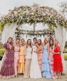 a group of women standing next to each other under a floral covered arch at a wedding