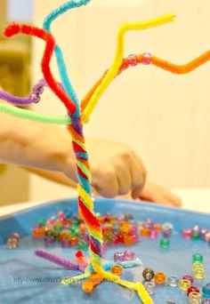 a child's hand is making a tree made out of beads and plasticine