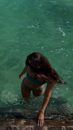 a woman standing in the water next to a wooden dock with her hair blowing back