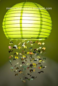 a green lantern hanging from the ceiling with small butterflies coming out of it to fly