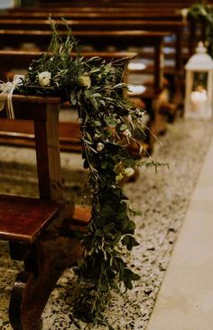 a wooden bench with flowers and greenery on the back is sitting in front of an empty pew