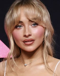 a close up of a woman with blonde hair and blue eyes wearing a diamond necklace