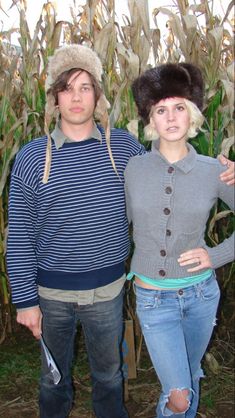 a man and woman standing next to each other in front of a cornfield