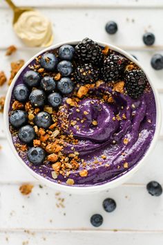 a bowl filled with blueberries and granola on top of a white table next to a spoon