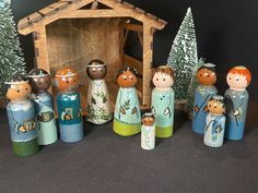 a group of wooden dolls standing in front of a nativity scene with pine trees