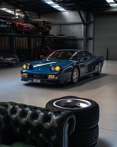 a blue sports car parked in a garage next to two black leather couches and other cars