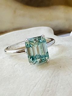 an emerald colored ring sitting on top of a white cloth