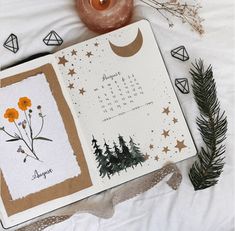 an open planner with flowers and plants on it next to a candle, pine branches and other items